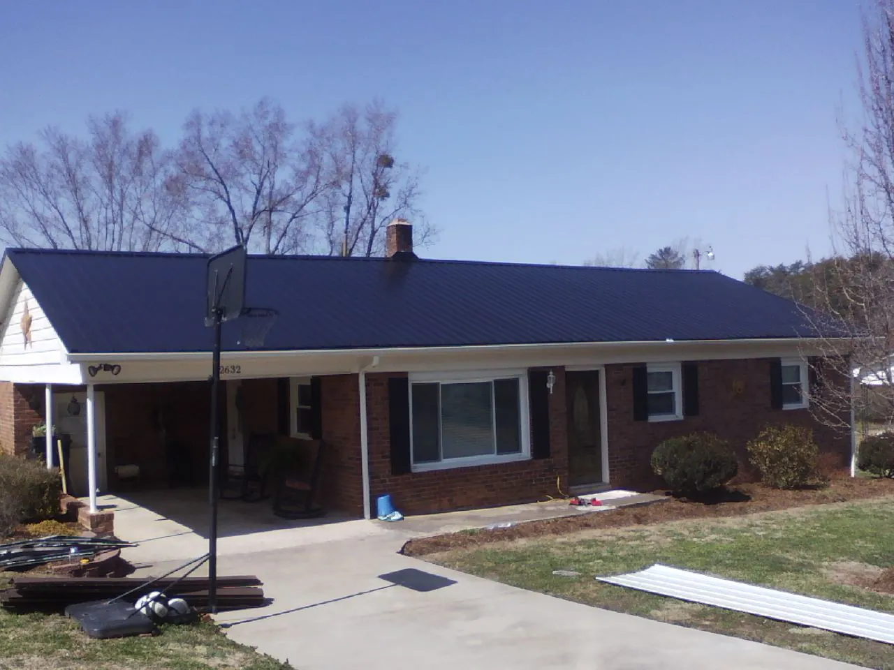 Finished dark blue metal roof on a brick ranch with a carport in Lowell