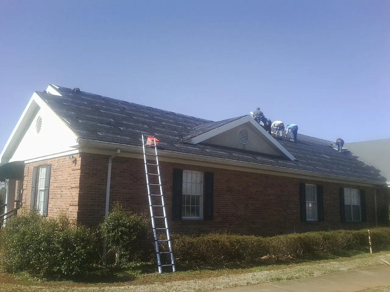 Crew tearing shingles off a brick ranch roof with a ladder set — Emergency Roof Repair work by our crew in Lowell