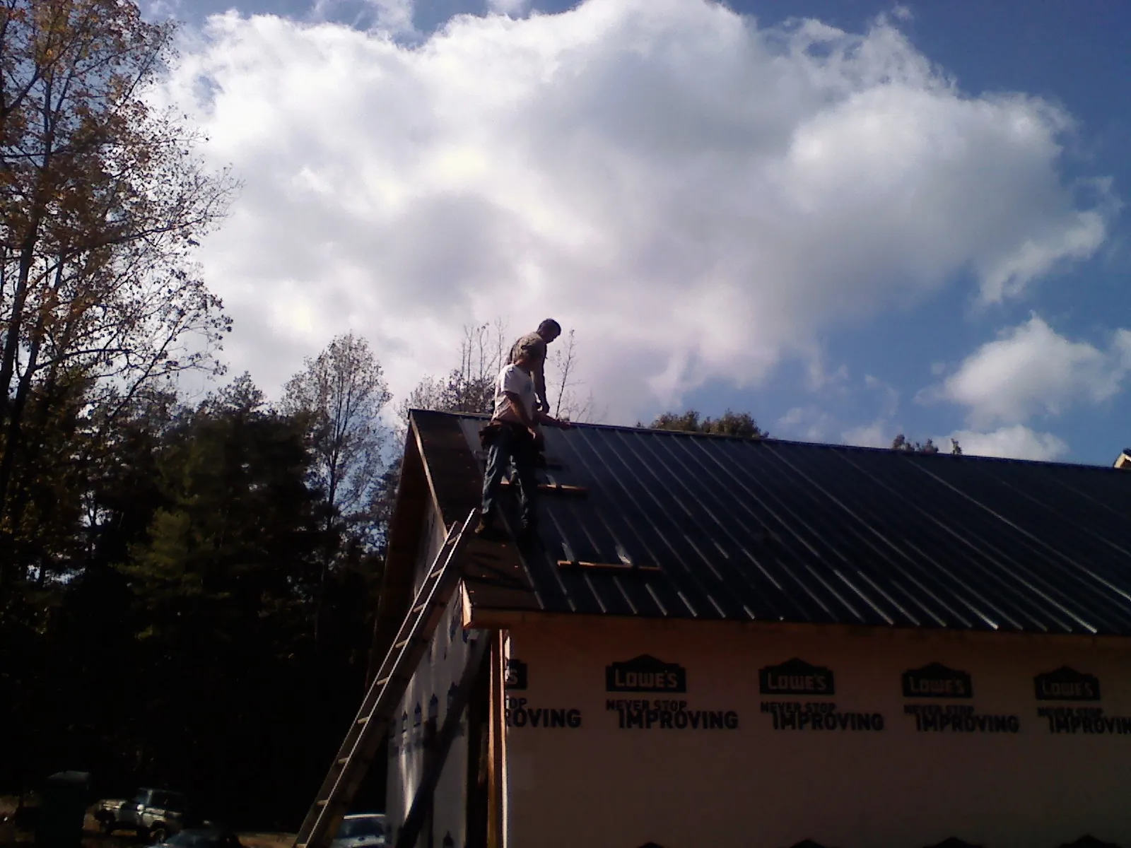 Roofer fastening dark metal panels high against a cloudy sky, from a Roof Inspection job in Lowell