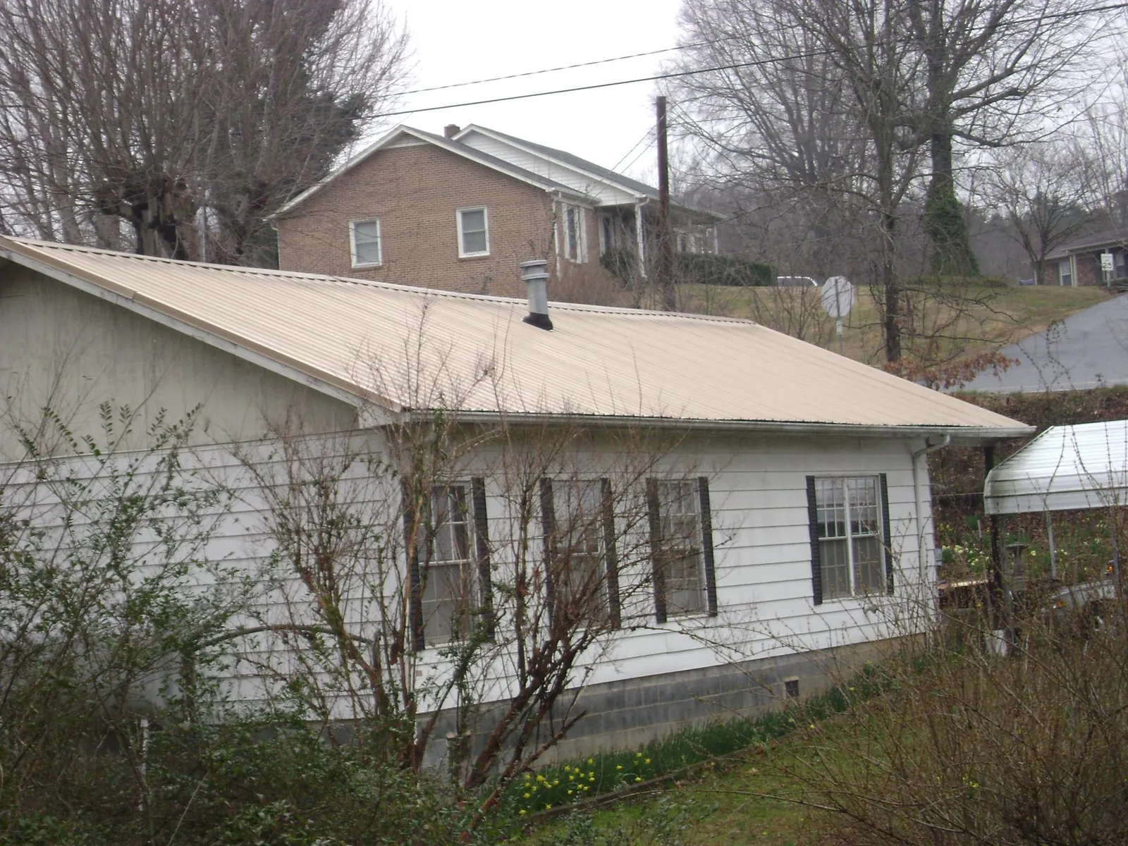 Tan metal roof on a white sided house set into a hillside — Commercial Roofing by Roofing Brothers in Lowell